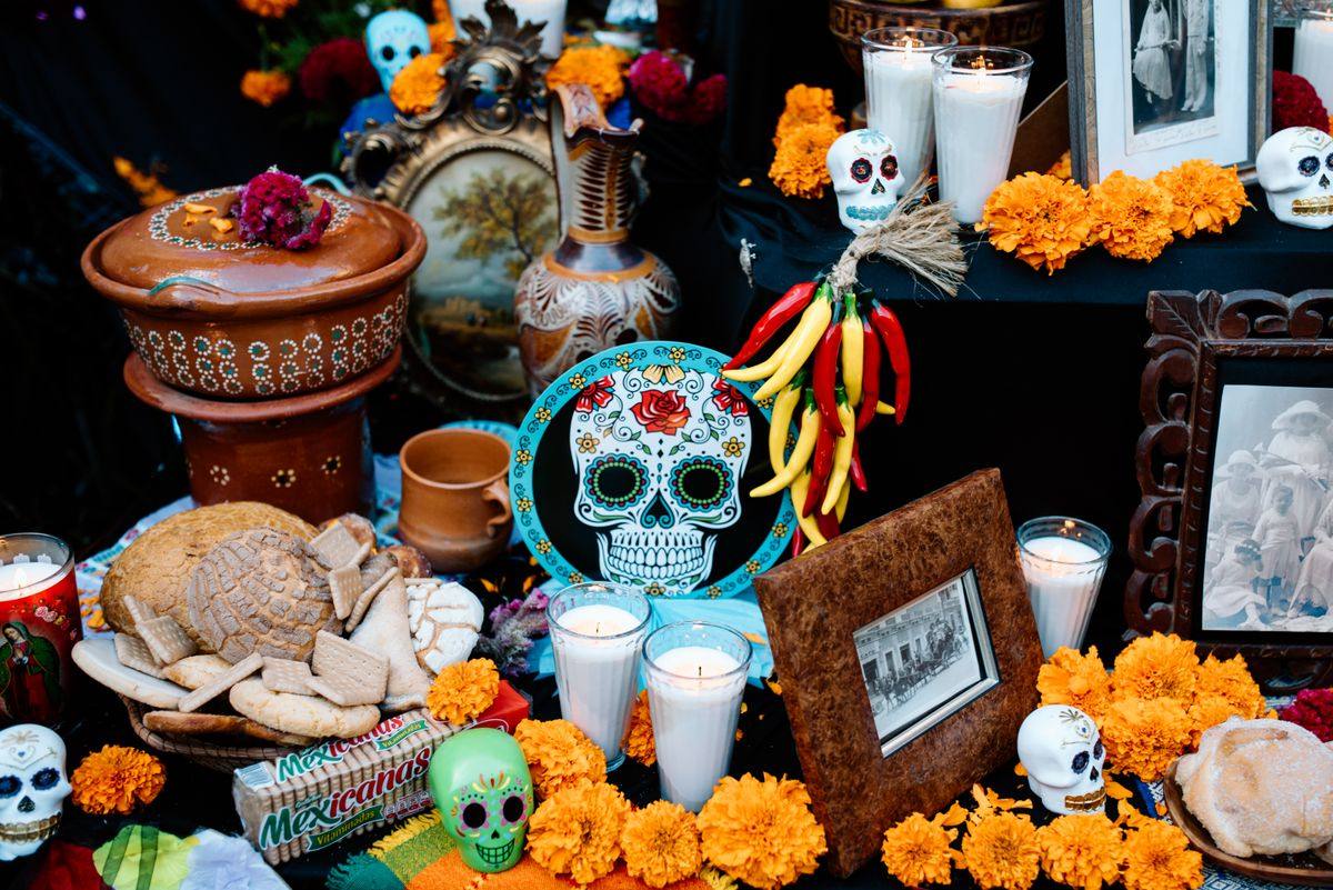 Autel avec bougies, fleurs orange, crânes décoratifs, photos encadrées et offrandes alimentaires