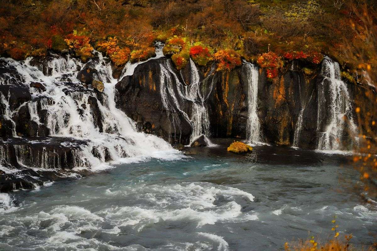 Cascade entourée de feuillages rouges et orange au bord d’une rivière