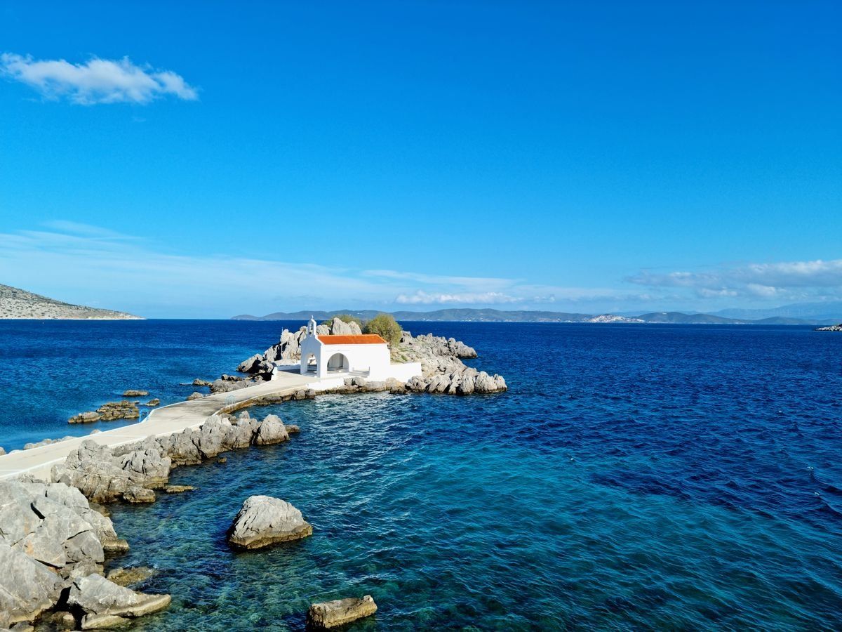 Petite chapelle blanche sur un îlot rocheux, reliée par une digue, au milieu d’une mer bleu profond