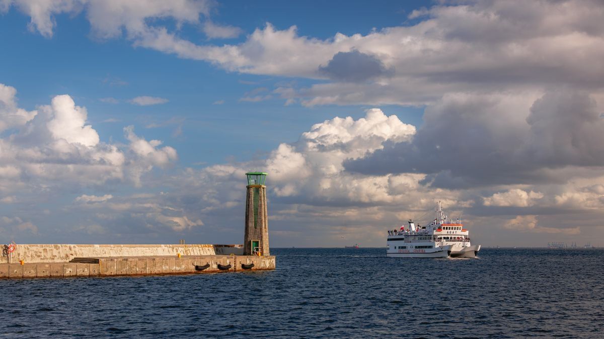 Phare au bout d’une jetée et ferry sur la mer sous de grands nuages