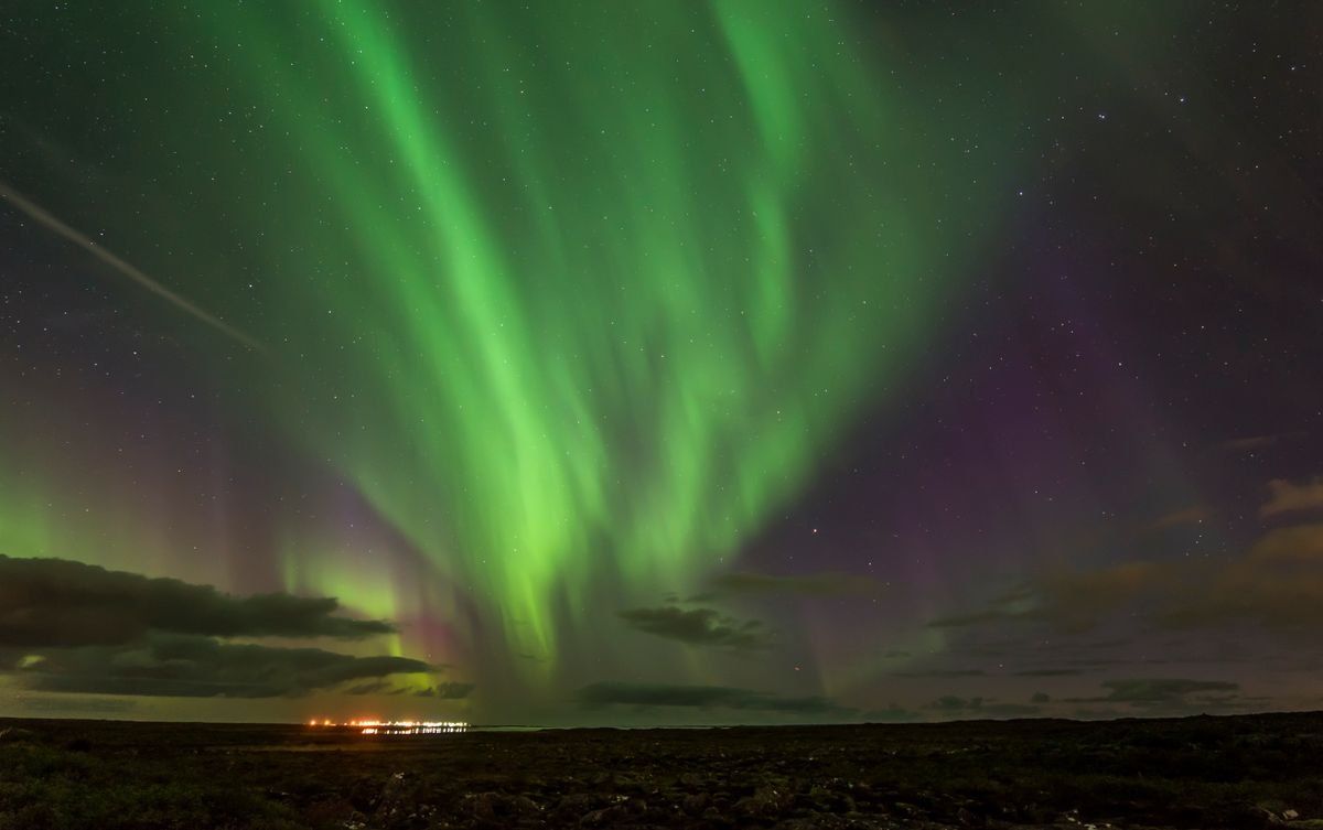 Rideaux d’aurores boréales vertes dans un ciel nocturne au-dessus d’un paysage sombre