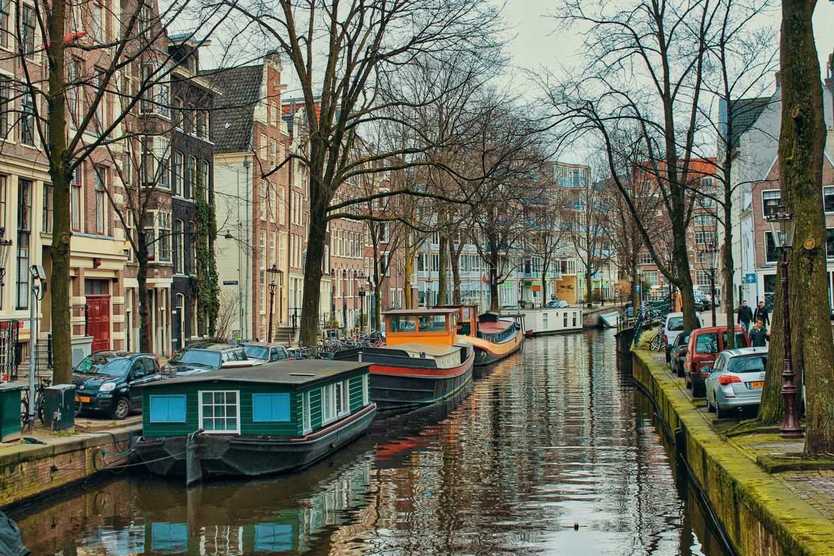 Canal bordé de péniches, voitures garées et maisons anciennes sous des arbres sans feuilles