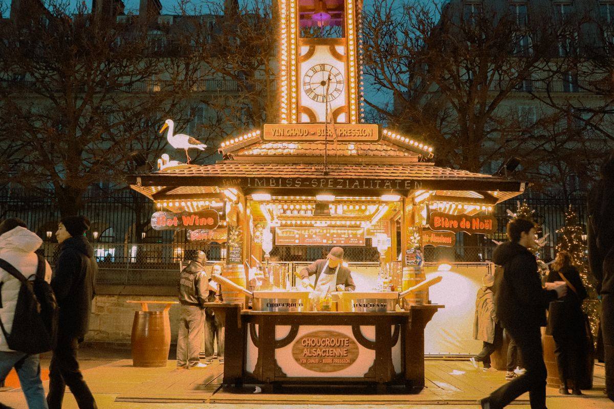 Chalet de marché de Noël illuminé à Paris avec horloge et passants autour du comptoir