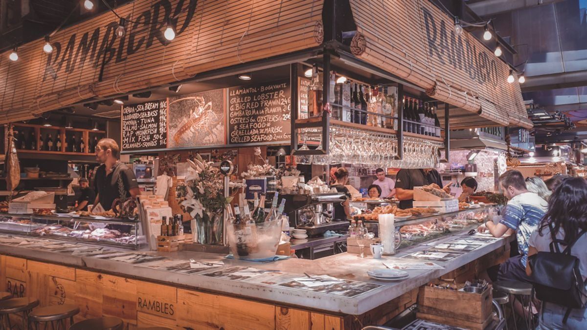 Comptoir de marché animé avec bouteilles, ardoises et clients assis