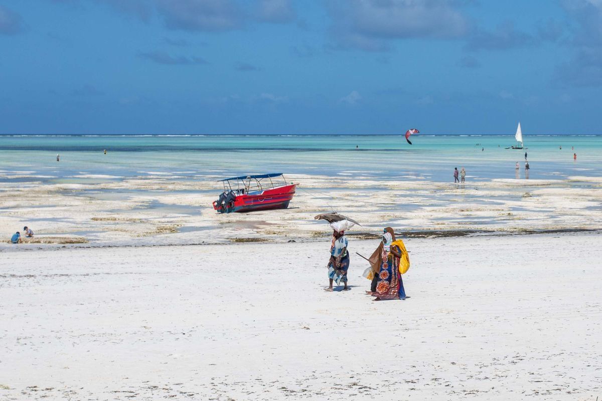 Deux femmes marchent sur une plage à marée basse près d’un bateau rouge