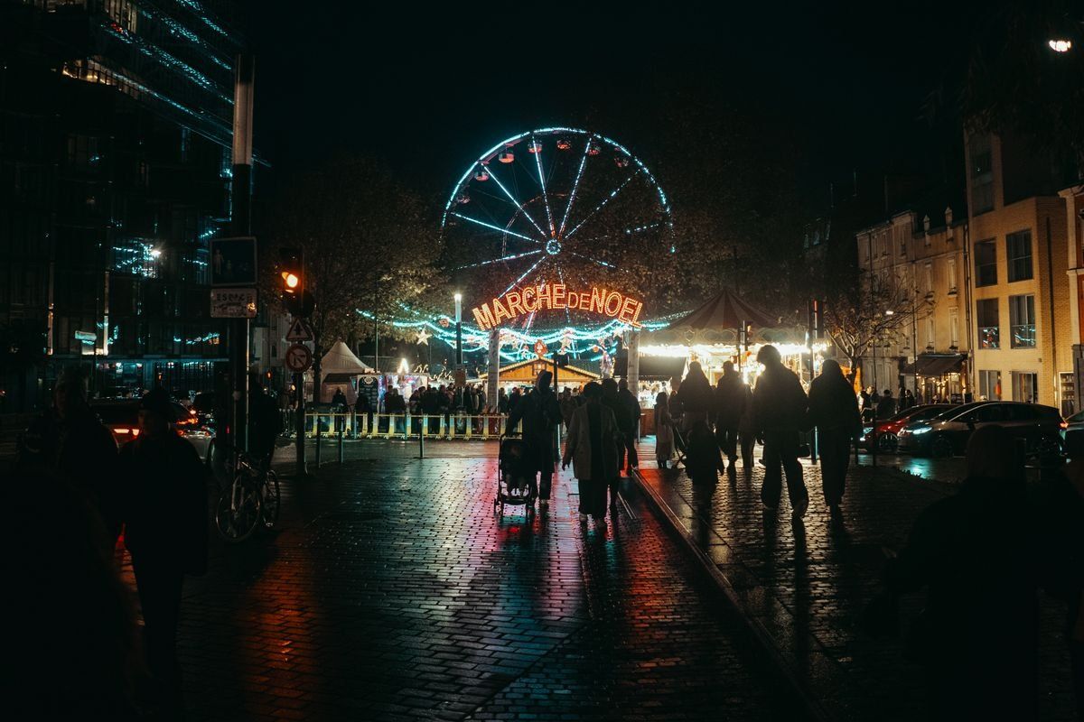 Marché de Noël nocturne à Rennes avec grande roue illuminée et passants sur les pavés mouillés