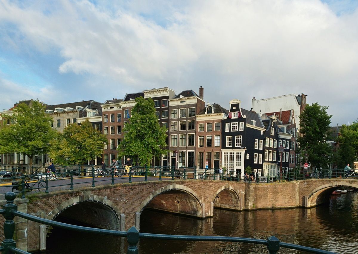 Pont en brique sur un canal avec maisons étroites et façades typiques d’Amsterdam
