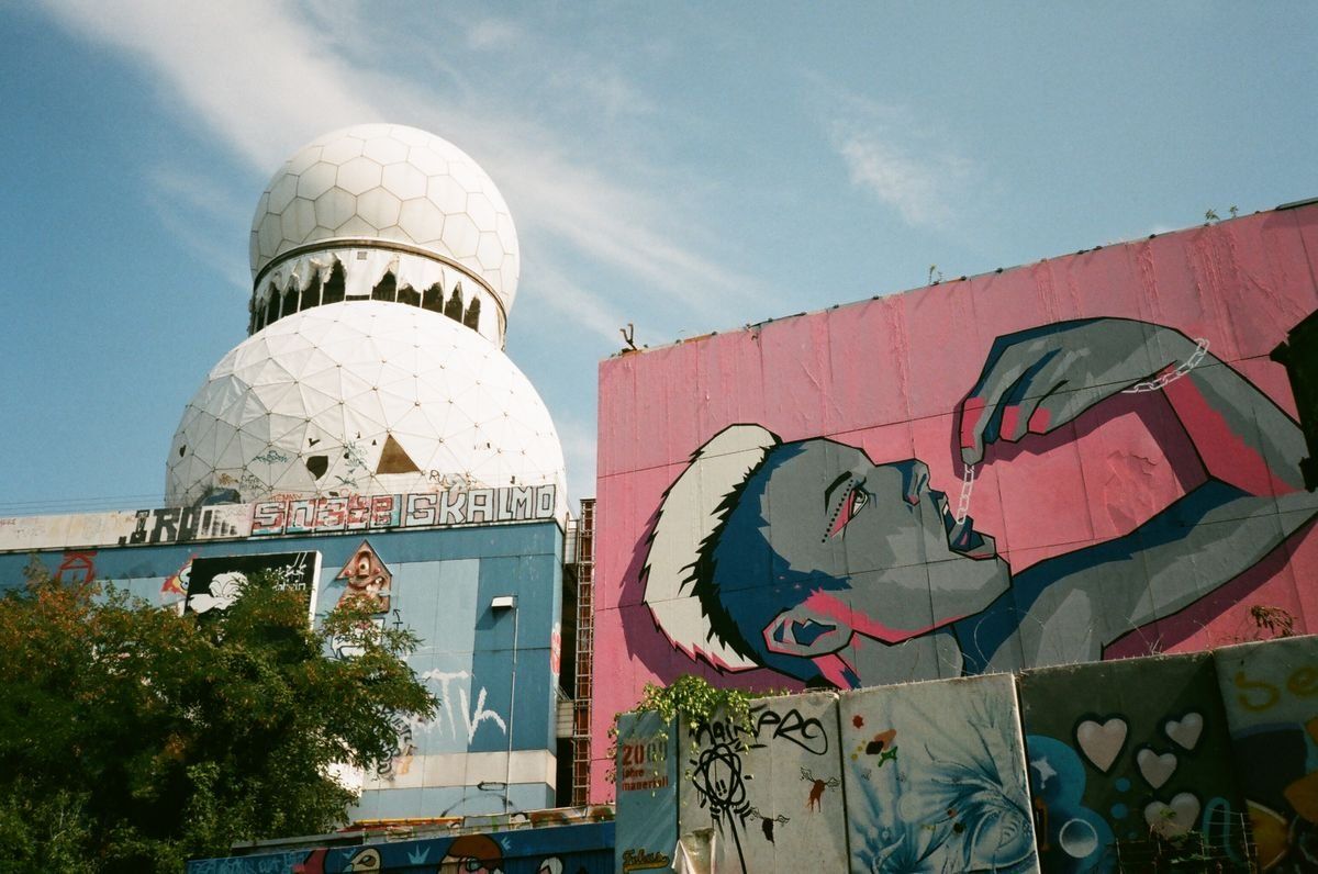 Radar blanc sphérique et grande fresque rose représentant un visage sur un bâtiment tagué