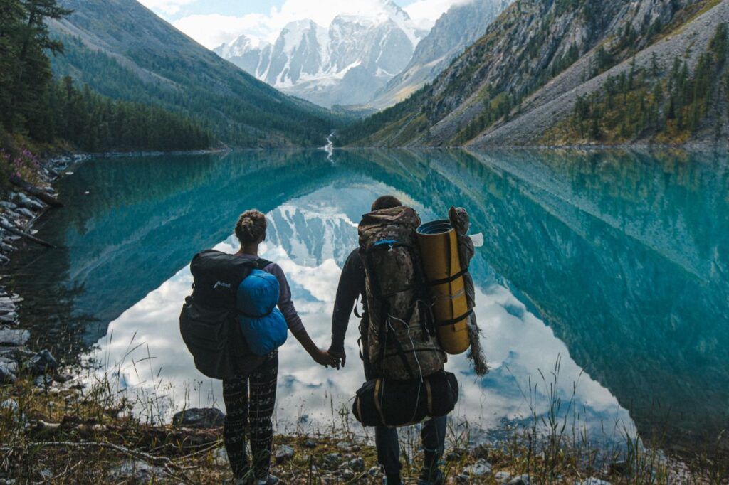 Deux randonneurs main dans la main face à un lac de montagne aux eaux turquoise