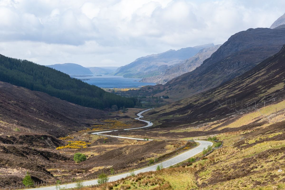 Route sinueuse dans une vallée des Highlands avec loch au loin