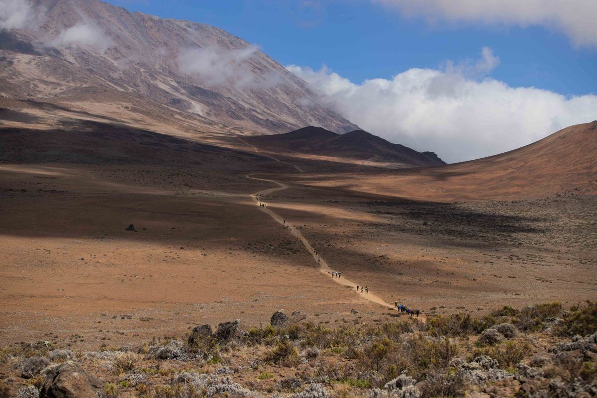 Sentier de trek serpentant dans un paysage aride avec quelques marcheurs au loin