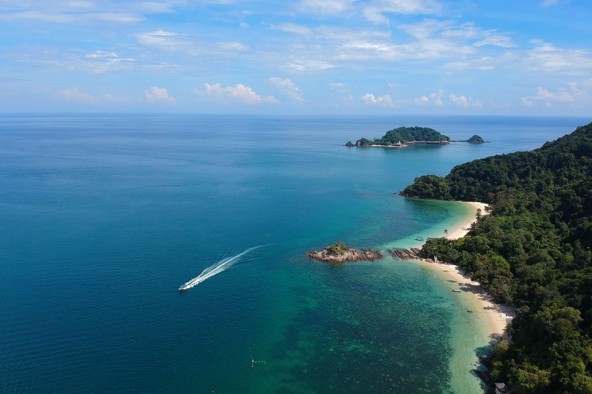 Vue aérienne d’une île tropicale entourée d’eau turquoise avec un bateau au large